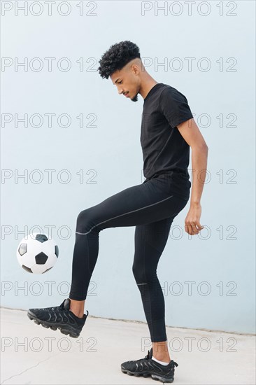 Black sportsman kicking football blue wall background