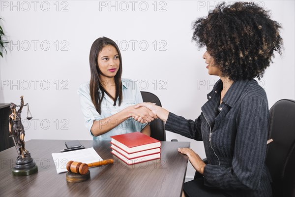 Black women shaking hands table with books smartphone statue document