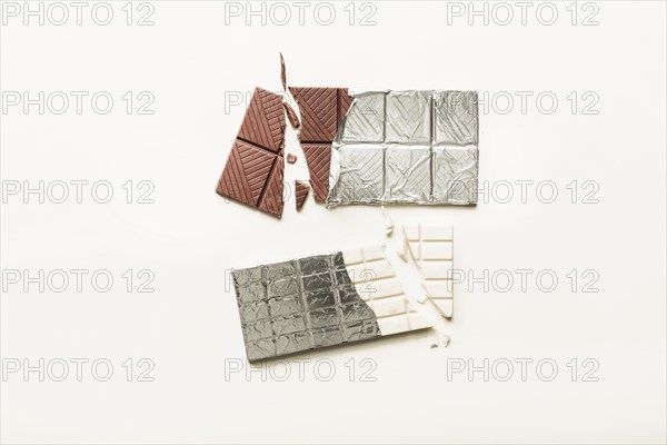 Broken white brown chocolate bar wrapped foil plain background
