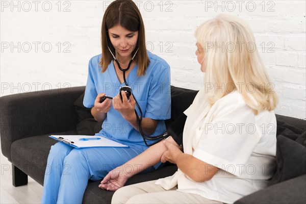 Caregiver checking old woman s blood pressure