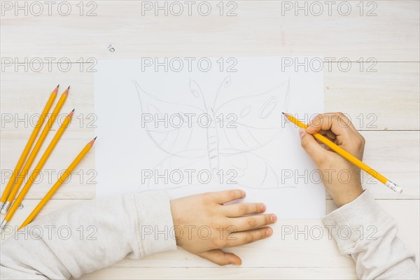 Child hand sketching butterfly with pencil wooden background