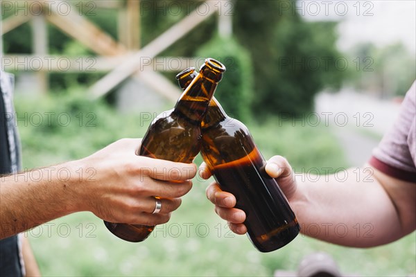 Close up friend s hand toasting brown beer bottles outdoors