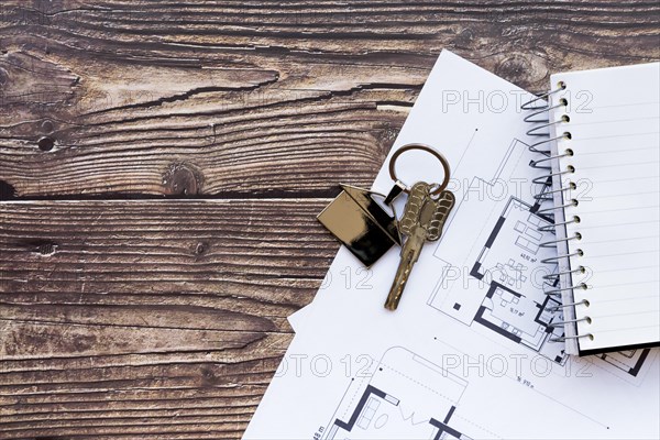 Close up house keys blueprint new home spiral notebook wooden textured backdrop