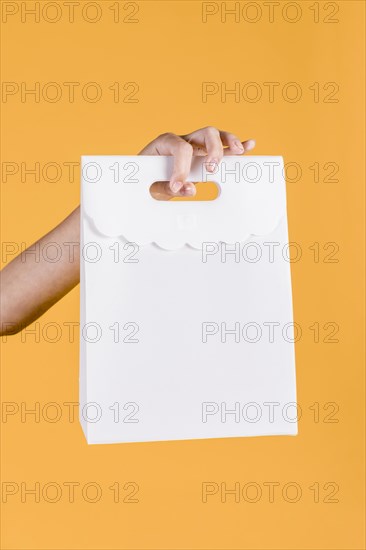 Close up human hand holding white paper bag yellow wall backdrop