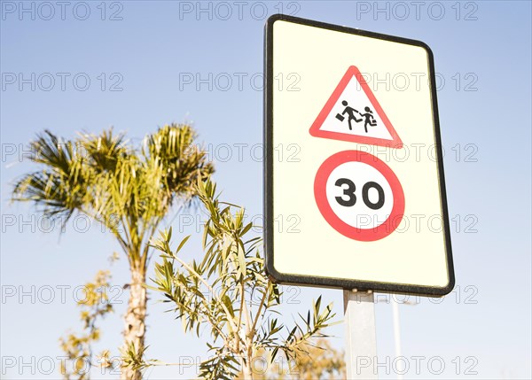 Close up pedestrians warning sign with 30 speed limit sign against green tree blue sky