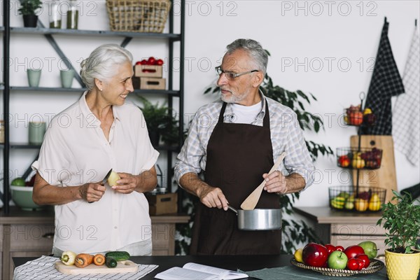 Close up senior couple preparing food kitchen looking each other