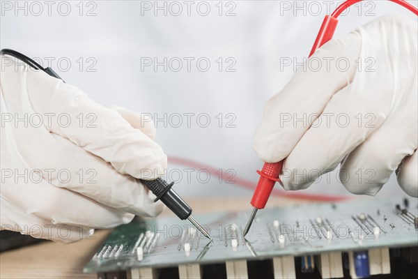 Close up technician hand examining computer circuit board with digital multimeter