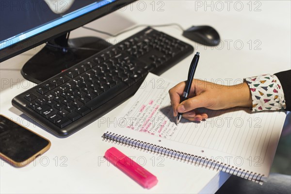 Crop hand writing notebook near computer