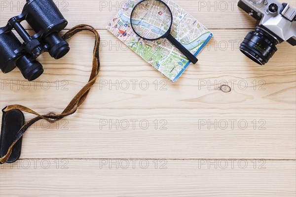 Elevated view binoculars magnifying glass map camera wooden surface