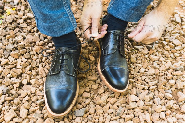 Elevated view man s foot pebble tying shoelace