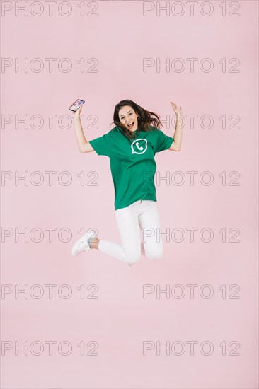 Excited woman with cellphone jumping pink background