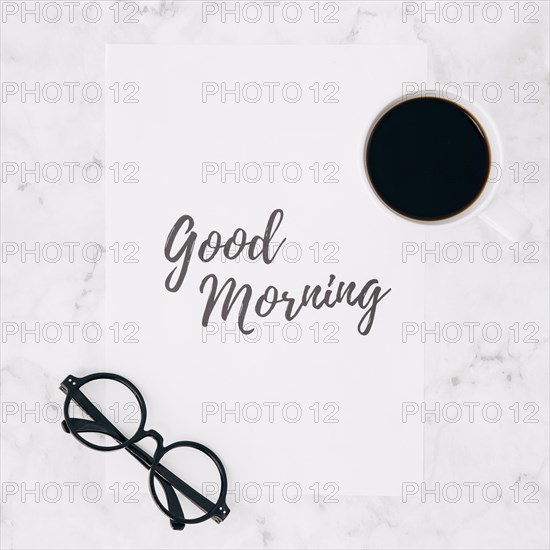 Eyeglasses coffee cup good morning text paper white marble textured backdrop