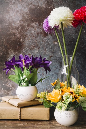 Fake flowers different type vase with wrapped gift boxes against grunge background