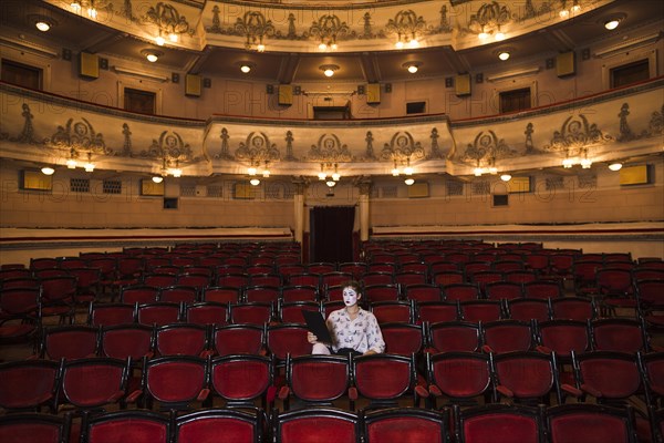 Female mime with manuscript sitting center auditorium