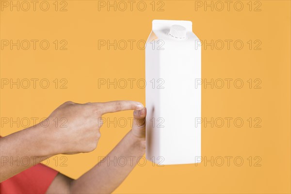 Female pointing finger white tetra pack against yellow backdrop