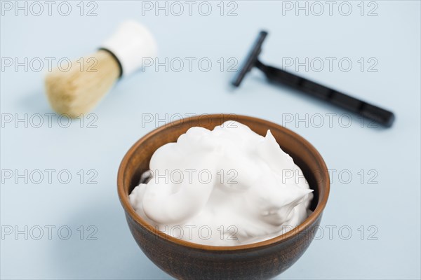 Foam wooden bowl front razor shaving brush against blue background