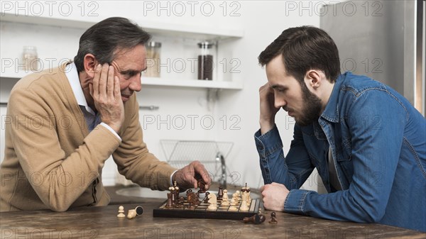 Front view father son playing chess kithcen