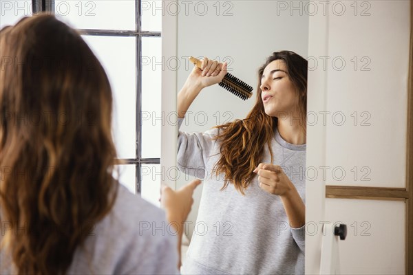 Front view happy woman singing into hairbrush home