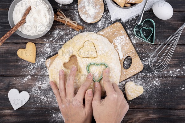 Hands making valentines day heart shaped cookies with kitchen utensils