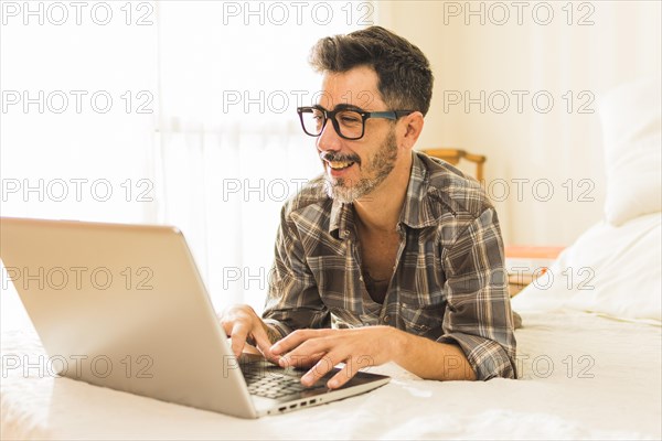 Happy man lying cozy bed using laptop