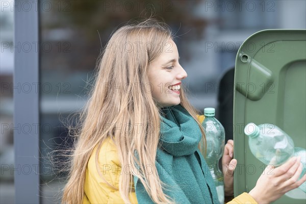 Young woman with plastic bottles at a green rubbish bin as environmental protection