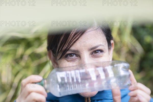Woman with a plastic bottle in front of a wall of plants Environmental protection