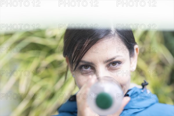 Woman with a plastic bottle in front of a wall of plants Environmental protection