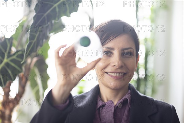 Woman surrounded by green plants holding up a plastic bottle