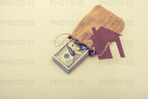 Paper house placed beside a bundle of US dollar banknote