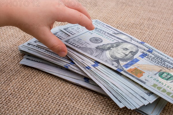 Toddler hand holding banknote bundle of US dollar on a linen canvas background