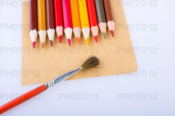 Color pencils and a brush placed on brown sheet of paper