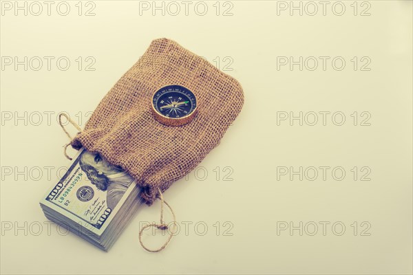 Compass and bundle of US dollarin a sack on a white background