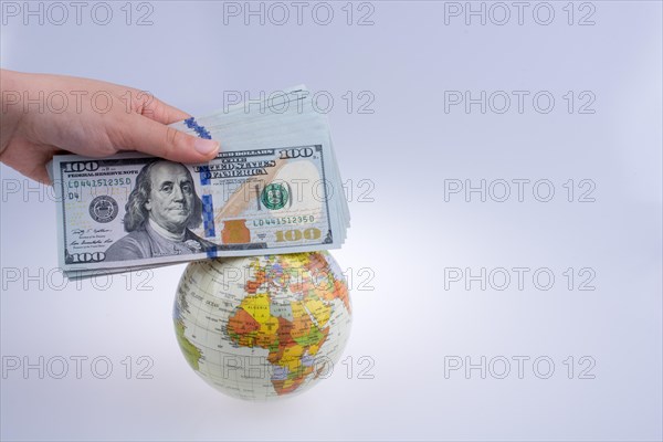 Human hand holding American dollar banknotes by the side of a model globe on white background