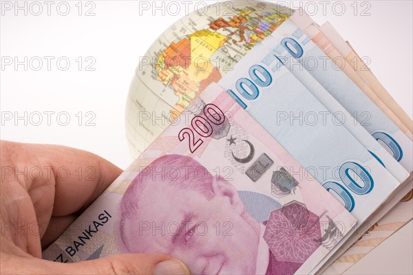 Hand holding Turkish Lira banknotes by the side of a model globe on white background