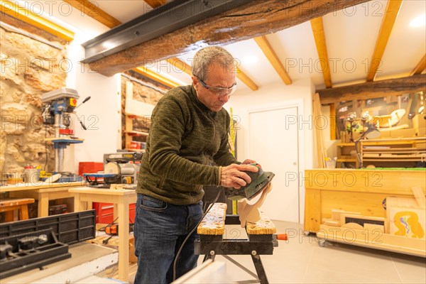Concentrated carpenter polishing a piece of wood using electric tool in a workshop