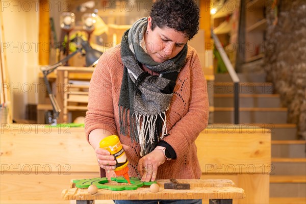 A woman using glue to attach painted wooden pieces in a workshop