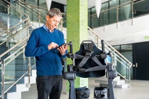 Mechanical exoskeleton computer engineer looking at the robot with a tablet. Physiotherapy in a modern hospital: Robotic skeleton. Physiotherapy Rehabilitation Scientists