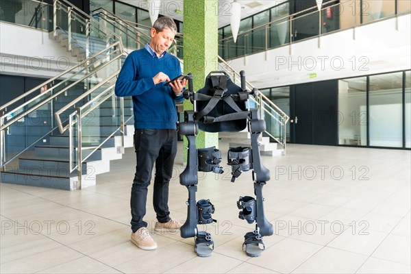 Mechanical exoskeleton computer engineer looking at the robot with a tablet. Physiotherapy in a modern hospital: Robotic skeleton. Physiotherapy Rehabilitation Scientists