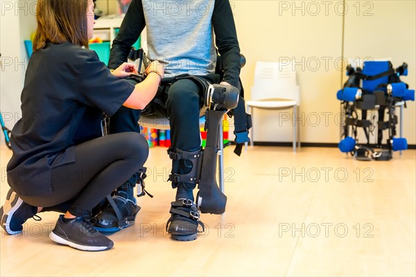 Mechanical exoskeleton. Physiotherapy in a modern hospital: Female physiotherapist helping disabled person with robotic skeleton with tapes. Futuristic rehabilitation