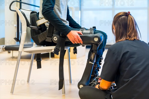 Mechanical exoskeleton. Physiotherapy in a modern hospital: Female physiotherapist placing tapes on disabled person with robotic skeleton. Futuristic rehabilitation