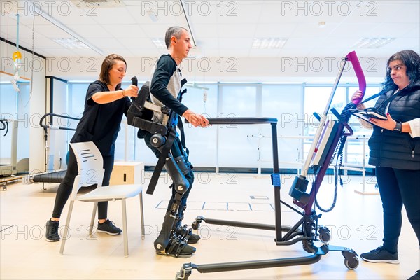 Mechanical exoskeleton. Physiotherapy medical assistant lifting disabled person with robotic skeleton to get up. Futuristic rehabilitation