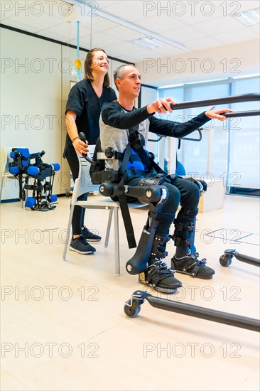 Mechanical exoskeleton. Female physiotherapy doctor assistant lifting disabled person with robotic skeleton to get up. Futuristic rehabilitation