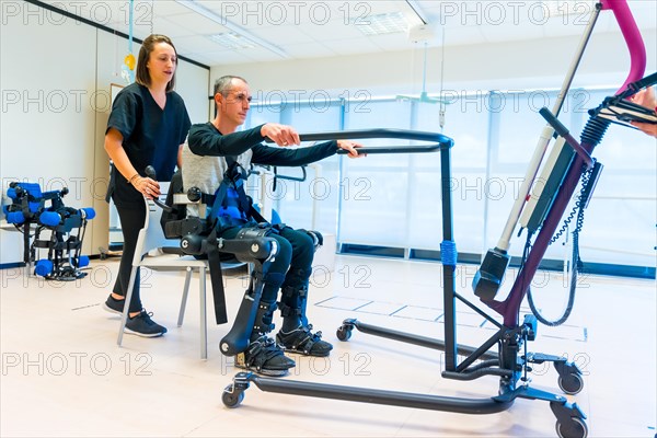 Mechanical exoskeleton. Female physiotherapy doctor assistant lifting disabled person with robotic skeleton to get up. Futuristic rehabilitation