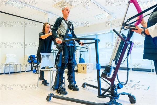 Mechanical exoskeleton. Female physiotherapy medical assistant lifting disabled person with robotic skeleton. Futuristic rehabilitation