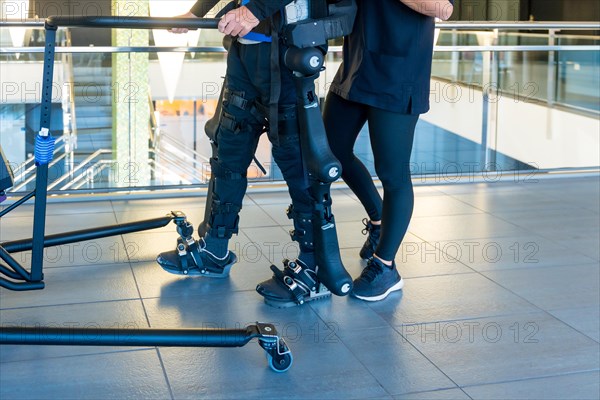 Mechanical exoskeleton. Female physiotherapy doctor helping unrecognizable disabled person with robotic skeleton to walk. Futuristic rehabilitation