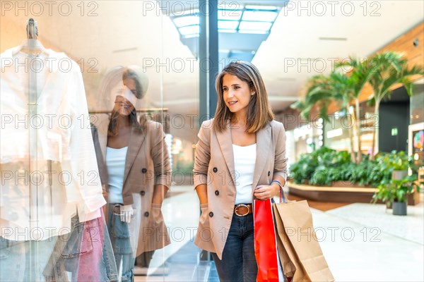 Woman looking at clothes through the window of a shop while walking along a mall