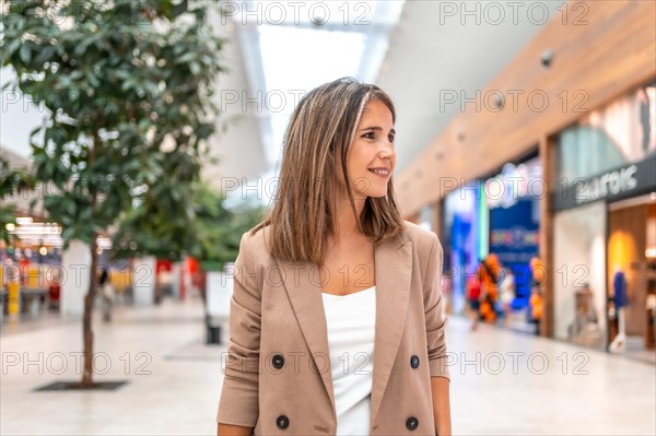 Woman walking along a indoor shopping mall with trees and shops inside