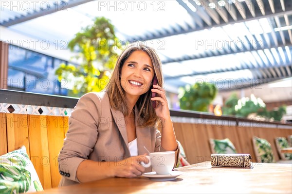 Happy mature woman drinking coffee and talking to the phone sitting on a cafeteria