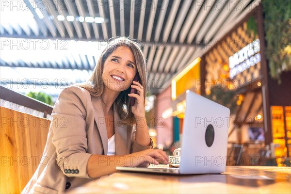 Elegant businesswoman using laptop and talking to the mobile sitting on a cafeteria in a mall