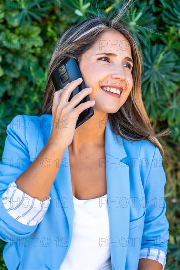 Vertical close-up portrait of a casual businesswoman talking to the phone in a green area